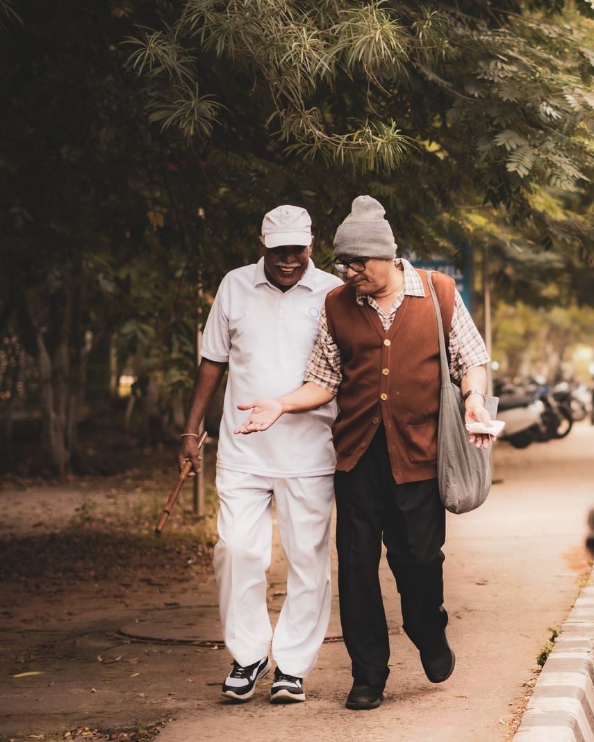 Two elderly friends walking arm in arm under trees on a quiet morning